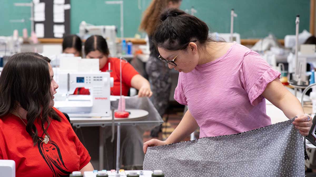 A woman holds a piece of fabric while another woman looks on.