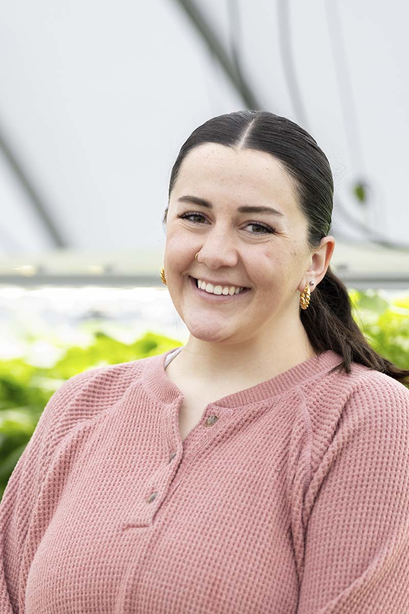 A portrait of a woman with potato plantlets in the background.