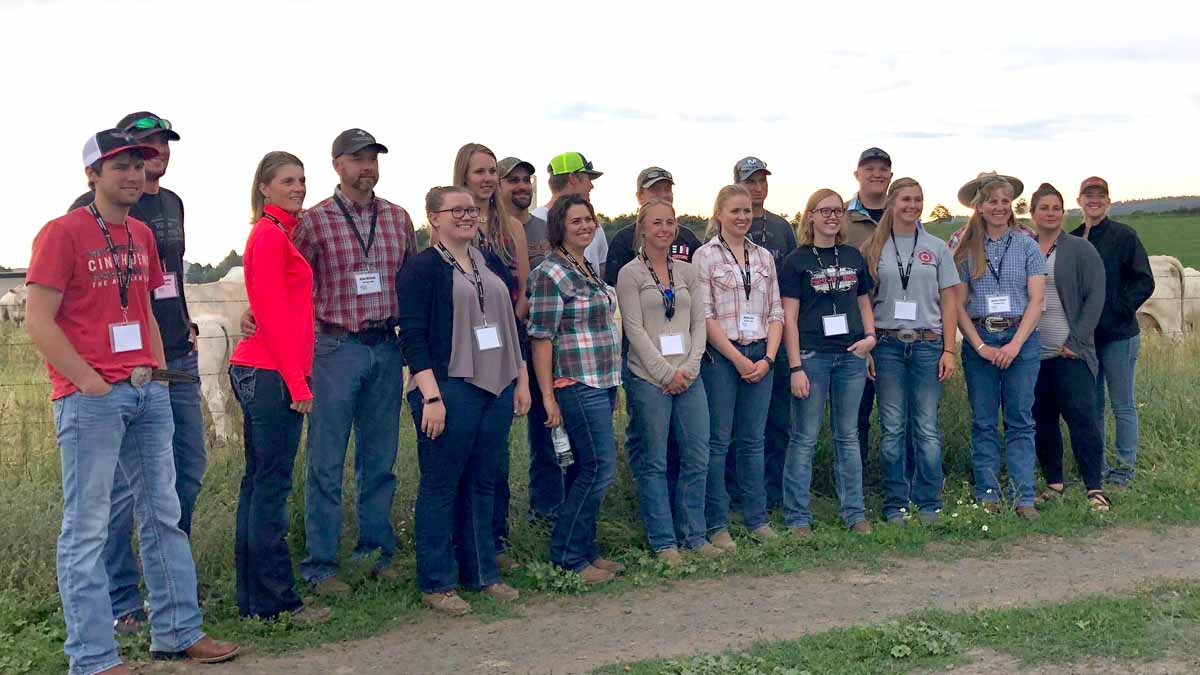 A group of men and women pose for a photo in front of a pasture of cattle.