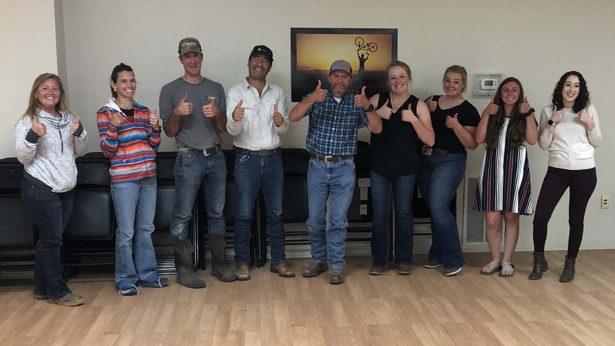 A group of nine men and women smile with thumbs up.