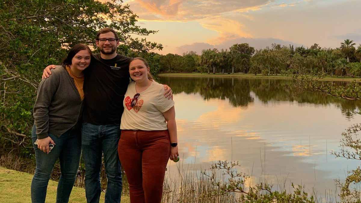 A man and two women stand next to a body of water.