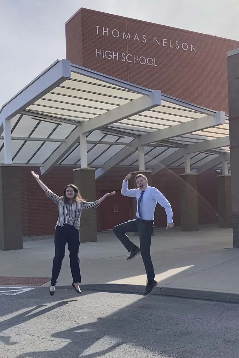 A man and two women jump in the air next to a high school.