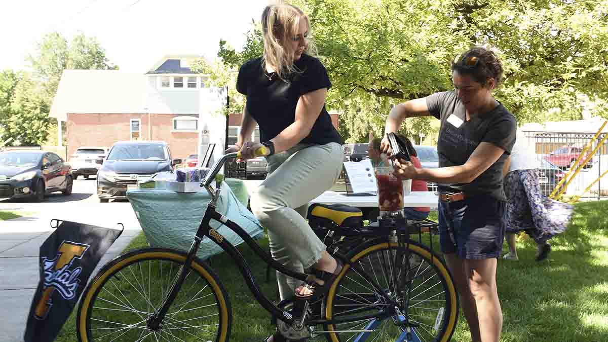 A woman on a bike and another woman adding fruit to be mixed