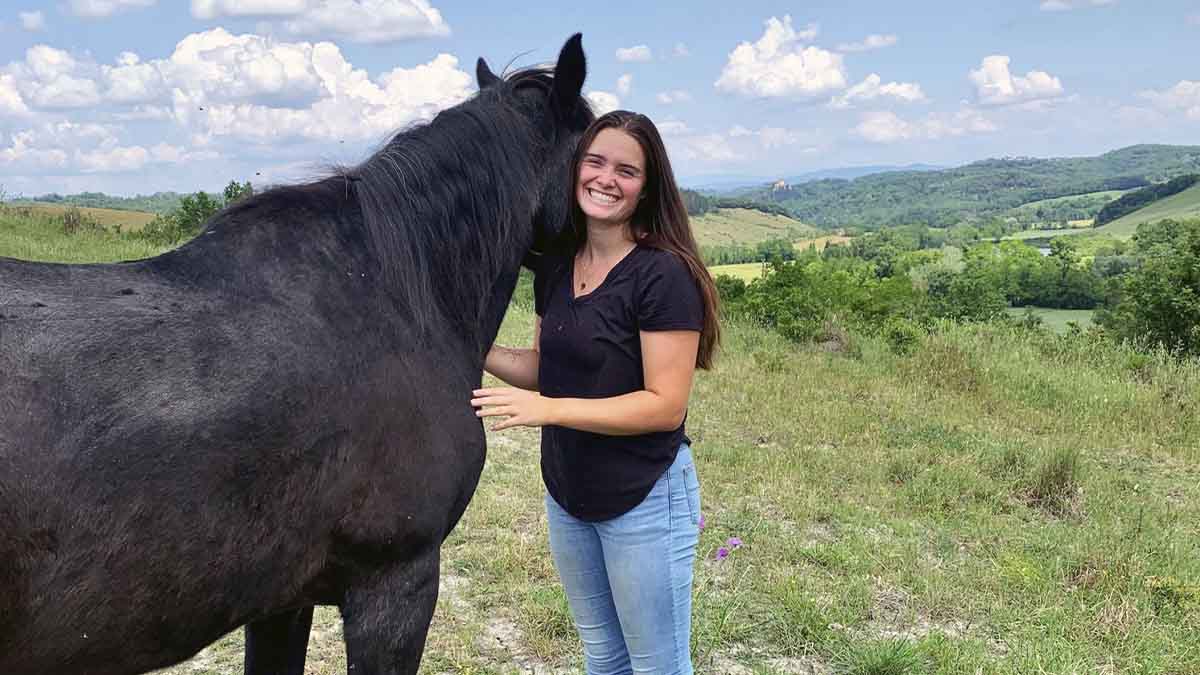 A woman standing next to a black horse in a field.