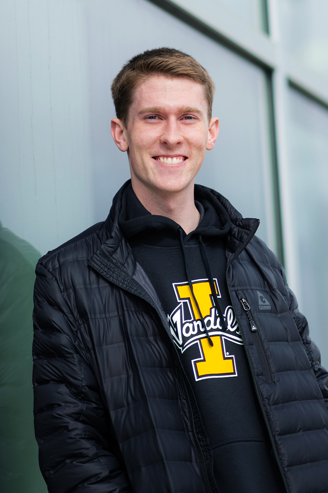 Young man wearing a black Vandals sweatshirt stands outside glass windows of Kibbie Dome.