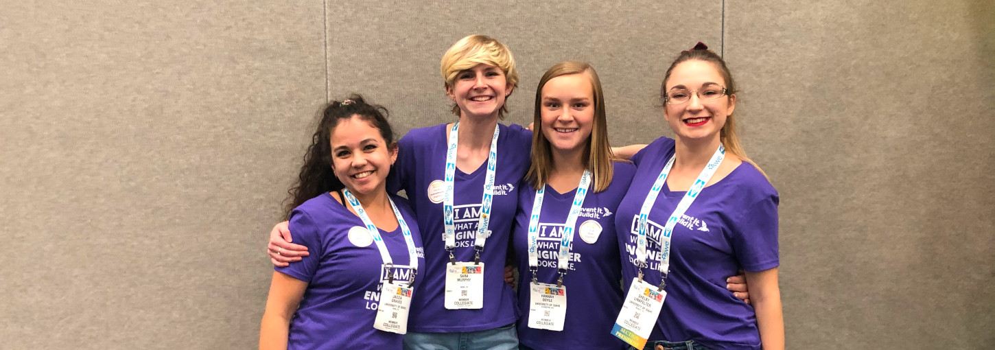 four students in matching shirts pose near wall