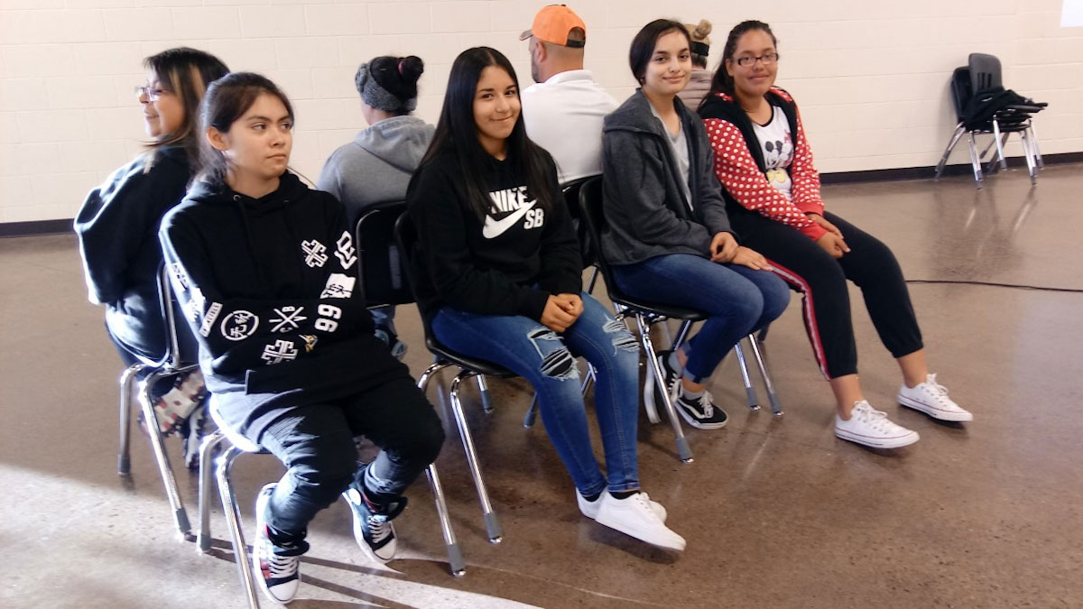 Four teen girls sit on chairs in a row.