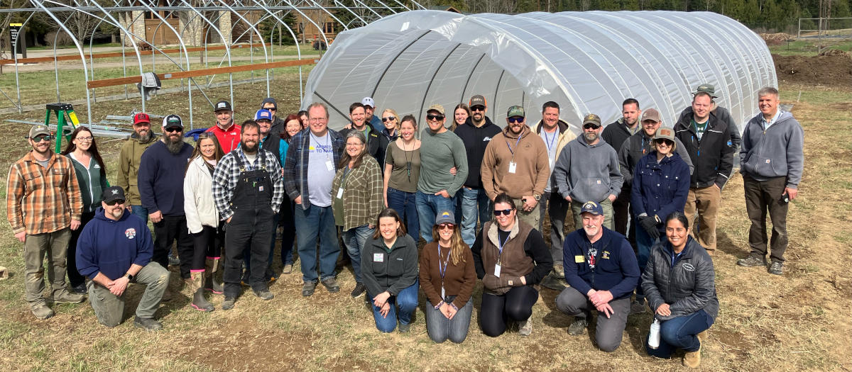 Large group poses in front of green houses.