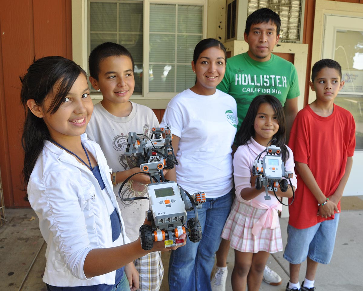 Children hold out LEGO robots as teens smile nearby.