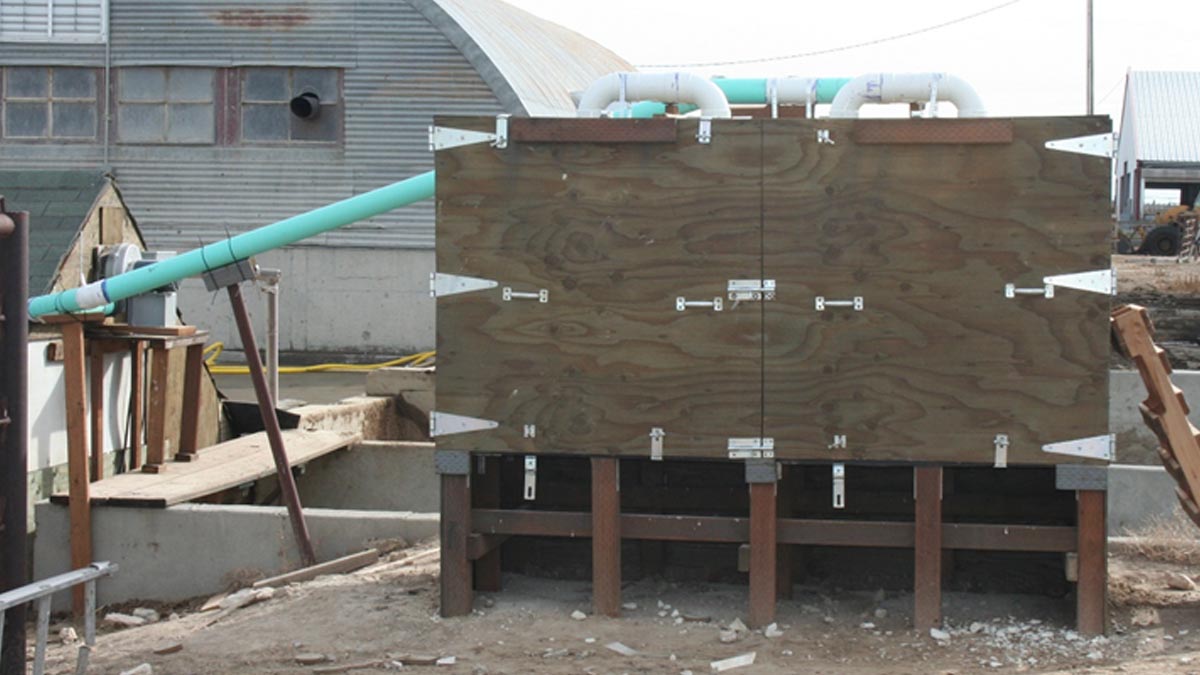 A raised plywood cabinet outdoors has PVC pipes going into it.