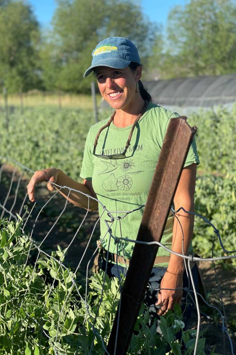 A woman stands amid a field of waist-high peas.