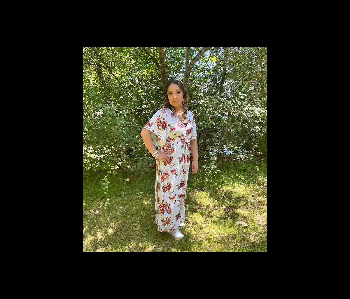 Angelica Gomez stands in front of bushes and trees.