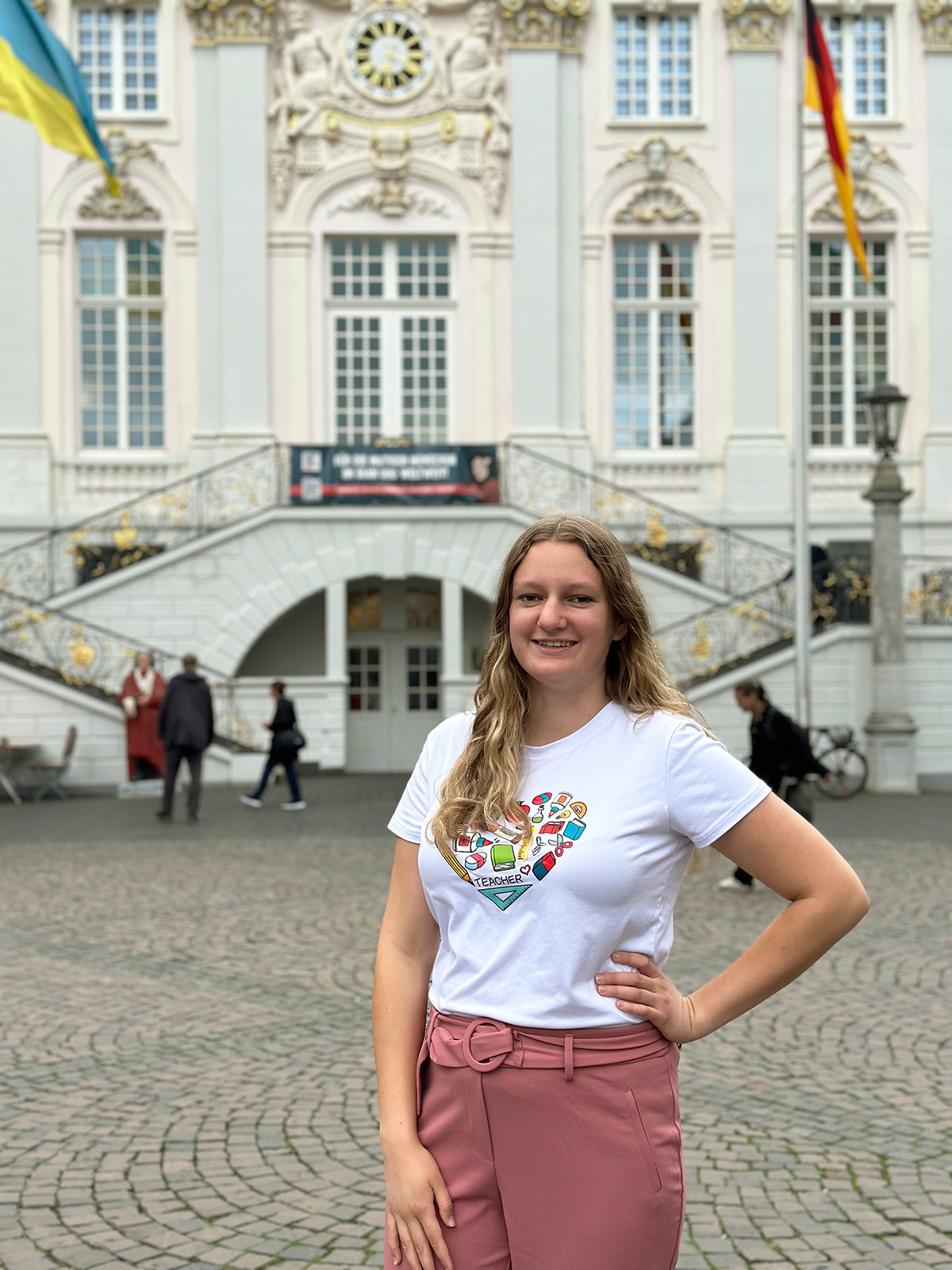 Woman standing in front of white building with flags.