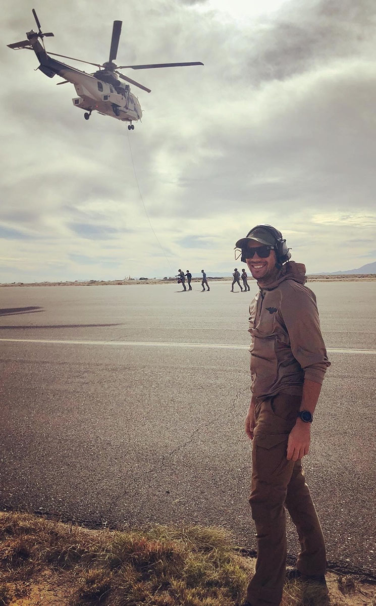 Man wearing sunglasses and headphones underneath helicopter.