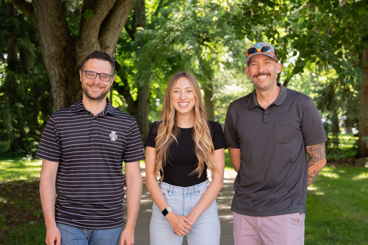Three people standing in front of trees.