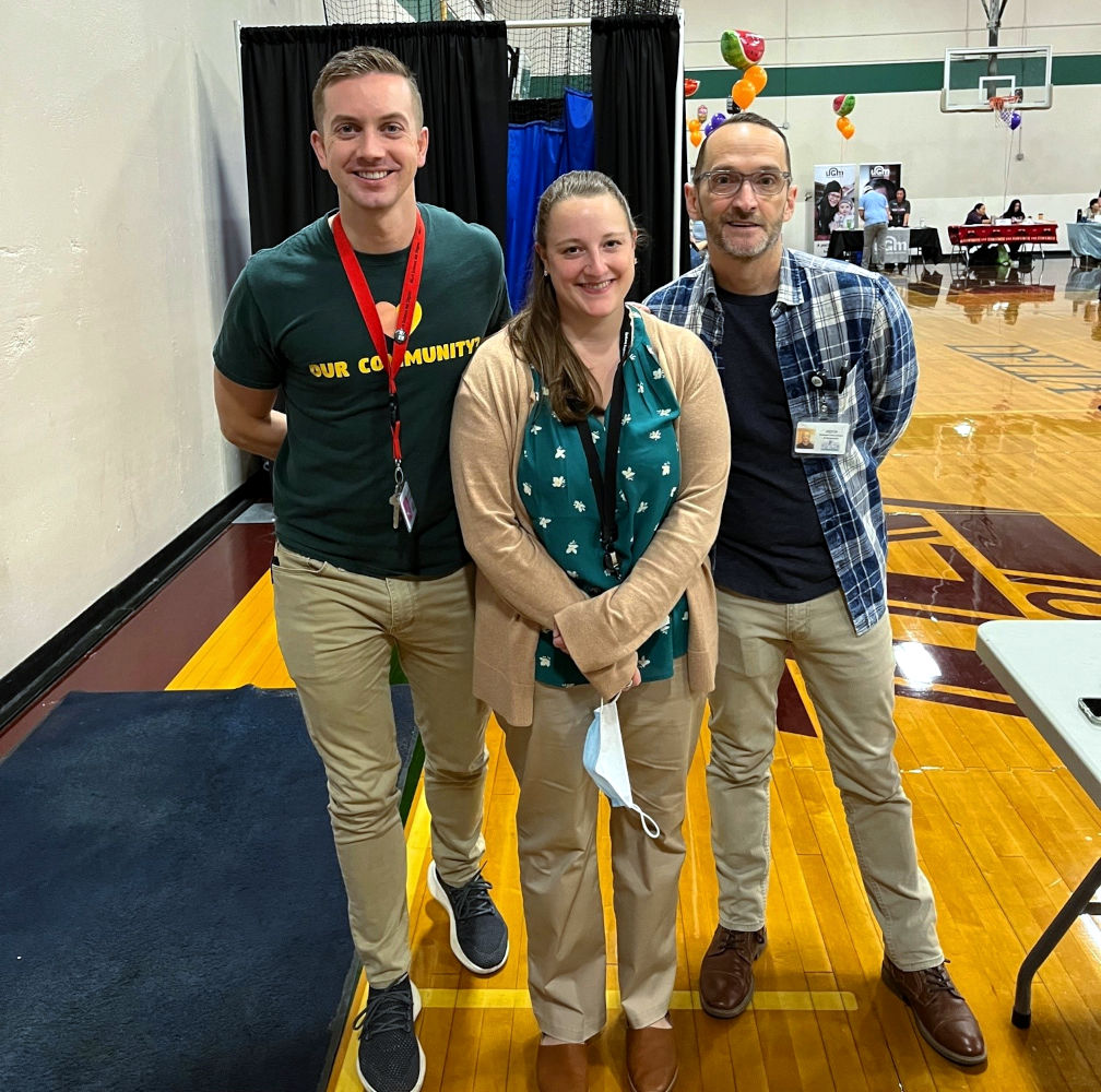 Three people at fair in school gym.