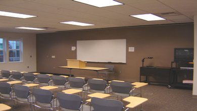 The whiteboard, seated desks, television, tables and projection equipment of LLC 144.